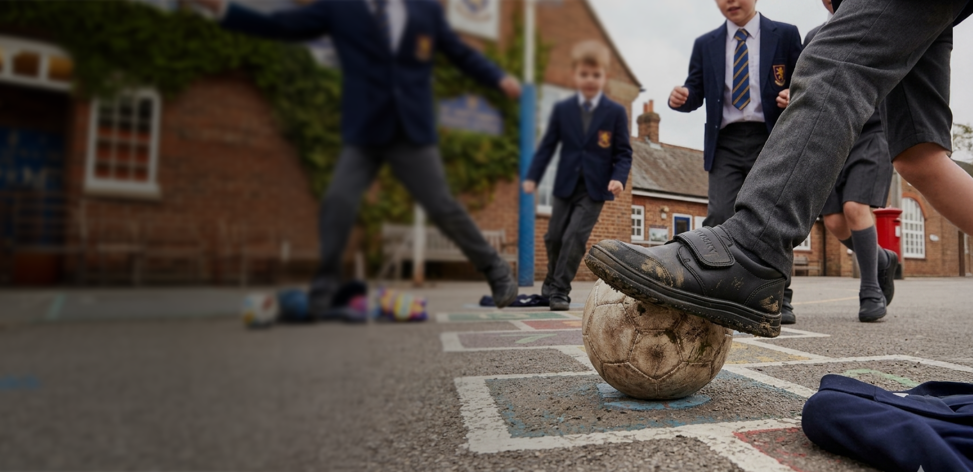 Children playing with a ball on a playground, with a building in the background.